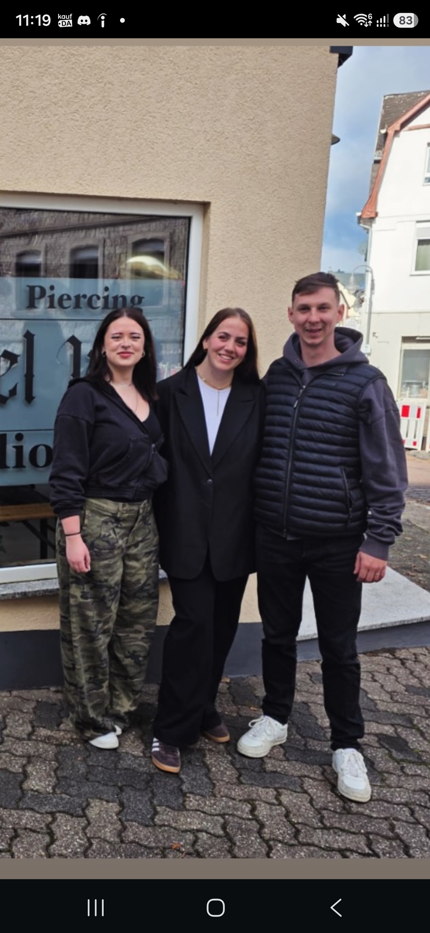 Jana, Lana und Rommel von links nach rechts vor dem Studioschaufenster mit Piercing-Schriftzug